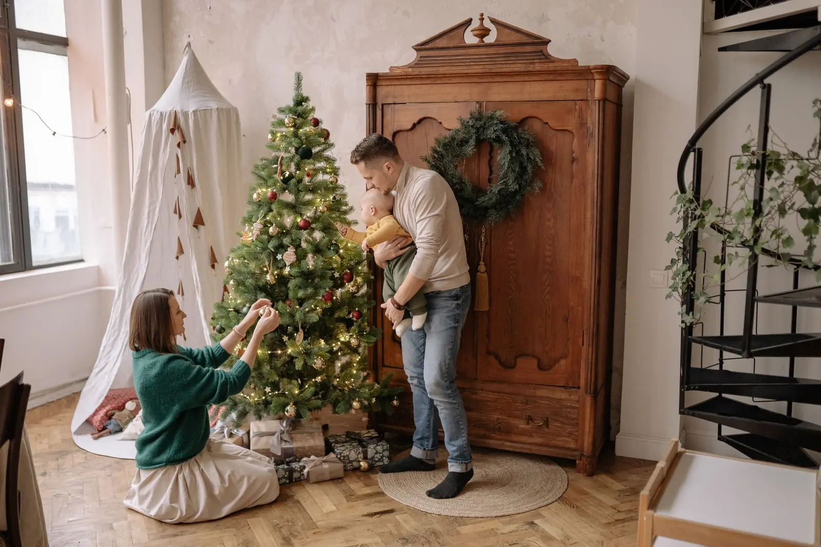 Familie med et lite barn pynter juletre hjemme i stua